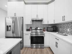 Kitchen with stainless steel appliances, white cabinetry, light wood finished floors, under cabinet range hood, and backsplash - 