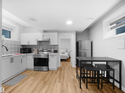 Legal basement suite Kitchen with appliances with stainless steel finishes, white cabinets, light countertops, light wood-style flooring, and decorative backsplash - 10913 159 Street, Edmonton, AB - Indoor Photo Showing Kitchen With Upgraded Kitchen