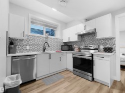 Legal basement suite Kitchen featuring stainless steel appliances, white cabinetry, under cabinet range hood, light wood-type flooring, and light stone countertops - 