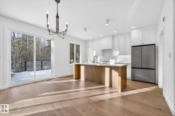 Kitchen featuring white cabinets, freestanding refrigerator, a kitchen island with sink, light wood-style flooring, and recessed lighting - 