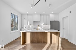 Kitchen featuring white cabinetry, light wood finished floors, a kitchen island with sink, tasteful backsplash, and freestanding refrigerator - 