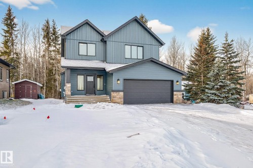 View of front of property featuring a garage, stone siding, board and batten siding, and a storage shed - 132 Heron Point Close, Rural Wetaskiwin County, AB - Outdoor With Facade