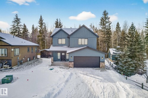 View of front of home featuring stone siding, a garage, and board and batten siding - 132 Heron Point Close, Rural Wetaskiwin County, AB - Outdoor With Facade