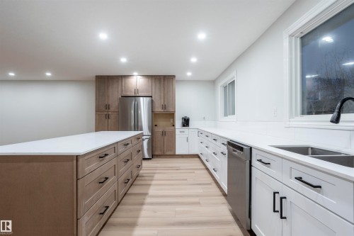 Kitchen with recessed lighting, appliances with stainless steel finishes, light stone counters, light wood-style floors, and brown cabinetry - 47 Manor Drive, Sherwood Park, AB - Indoor Photo Showing Kitchen