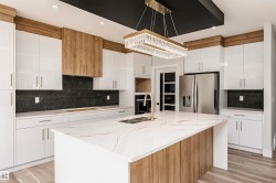 Kitchen with backsplash, white cabinetry, light stone counters, stainless steel refrigerator with ice dispenser, and an island with sink - 