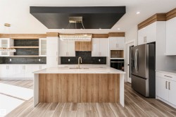 Kitchen featuring white cabinets, stainless steel refrigerator with ice dispenser, a center island with sink, light stone counters, and exhaust hood - 