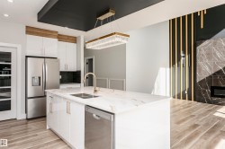 Kitchen with appliances with stainless steel finishes, white cabinetry, light stone counters, a high end fireplace, and a kitchen island with sink - 