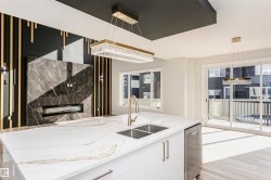 Kitchen with light stone countertops, stainless steel dishwasher, plenty of natural light, and hanging light fixtures - 