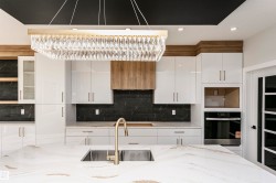 Kitchen with white cabinetry, backsplash, light stone countertops, stainless steel oven, and glass insert cabinets - 