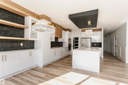 Kitchen featuring white cabinetry, decorative light fixtures, tasteful backsplash, a kitchen island with sink, and light wood-style floors - 