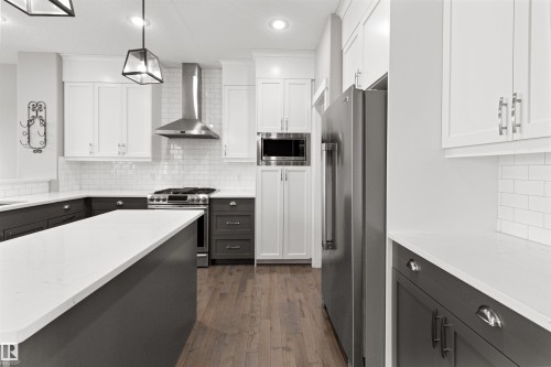 Kitchen with backsplash, appliances with stainless steel finishes, wall chimney range hood, dark wood-style flooring, and decorative light fixtures - 107 Cresthaven Grove, Ardrossan, AB - Indoor Photo Showing Kitchen With Upgraded Kitchen