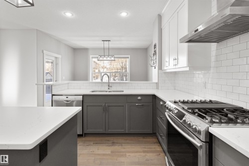 Kitchen featuring stainless steel appliances, wall chimney exhaust hood, light stone counters, backsplash, and light wood-style flooring - 107 Cresthaven Grove, Ardrossan, AB - Indoor Photo Showing Kitchen With Double Sink With Upgraded Kitchen