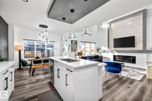 Kitchen featuring white cabinets, decorative light fixtures, a glass covered fireplace, open floor plan, and light stone counters - 5304 Kimball Place, Edmonton, AB - Indoor Photo Showing Kitchen With Fireplace With Double Sink