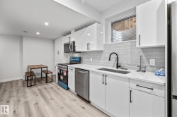 Kitchen featuring tasteful backsplash, white cabinetry, stainless steel appliances, light wood-style floors, and light stone countertops - 
