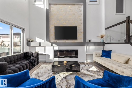 Living room featuring a glass covered fireplace, healthy amount of natural light, wood finished floors, and a towering ceiling - 5304 Kimball Place, Edmonton, AB - Indoor Photo Showing Living Room With Fireplace