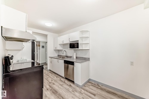 Kitchen featuring black appliances, open shelves, under cabinet range hood, white cabinets, and light wood-style flooring - 4B 13230 Fort Road, Edmonton, AB - Indoor Photo Showing Kitchen With Double Sink