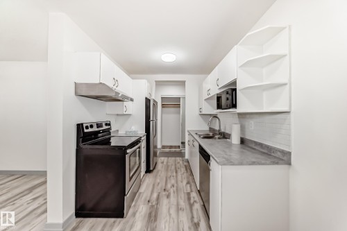 Kitchen featuring appliances with stainless steel finishes, open shelves, white cabinets, and light wood finished floors - 4B 13230 Fort Road, Edmonton, AB - Indoor Photo Showing Kitchen