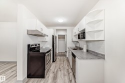 Kitchen featuring appliances with stainless steel finishes, open shelves, white cabinets, and light wood finished floors - 