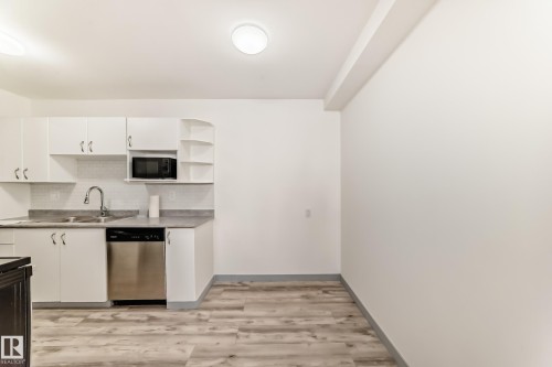 Kitchen featuring open shelves, white cabinetry, dishwasher, light wood finished floors, and black microwave - 4B 13230 Fort Road, Edmonton, AB - Indoor Photo Showing Kitchen With Double Sink