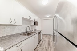 Kitchen featuring freestanding refrigerator, white cabinetry, light wood-style flooring, tasteful backsplash, and dishwasher - 
