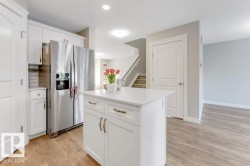 Kitchen featuring stainless steel refrigerator with ice dispenser, a kitchen island, white cabinets, light wood-style floors, and a textured ceiling - 