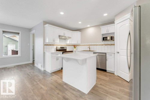Kitchen featuring appliances with stainless steel finishes, white cabinetry, decorative backsplash, light wood-style flooring, and a kitchen island - 1423 24 Street, Edmonton, AB - Indoor Photo Showing Kitchen With Stainless Steel Kitchen With Upgraded Kitchen