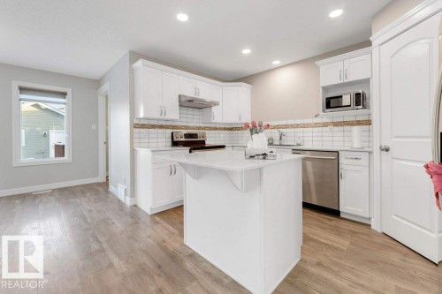 Kitchen featuring white cabinetry, stainless steel appliances, light wood finished floors, backsplash, and under cabinet range hood - 1423 24 Street, Edmonton, AB - Indoor Photo Showing Kitchen With Upgraded Kitchen