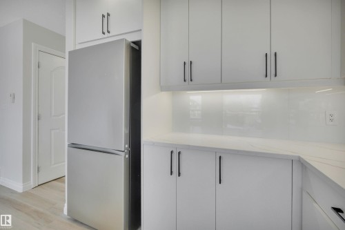 Kitchen featuring freestanding refrigerator, light stone countertops, light wood-style floors, and modern cabinets - 457 Aster Close, Leduc, AB - Indoor Photo Showing Kitchen
