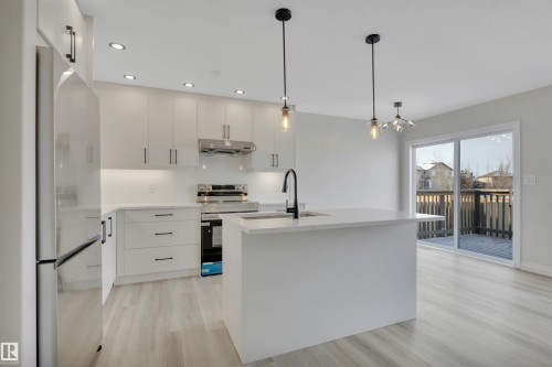 Kitchen with stainless steel electric range oven, freestanding refrigerator, pendant lighting, light wood-type flooring, and modern cabinets - 457 Aster Close, Leduc, AB - Indoor Photo Showing Kitchen With Upgraded Kitchen
