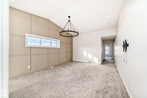 Unfurnished room featuring light carpet, lofted ceiling, a chandelier, and a decorative wall - 3249 Dixon Way, Edmonton, AB - Indoor Photo Showing Other Room