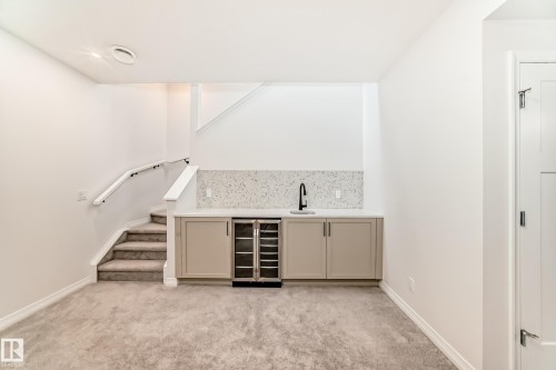 Indoor wet bar featuring beverage cooler, light carpet, light stone countertops, cream cabinets, and stairway - 3249 Dixon Way, Edmonton, AB - Indoor Photo Showing Other Room