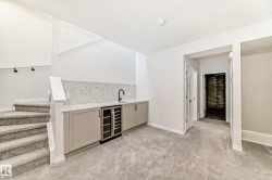 Indoor wet bar featuring beverage cooler, stairway, light carpet, light stone countertops, and gray cabinetry - 