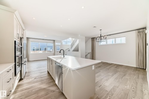 Kitchen with white cabinets, an island with sink, light wood-type flooring, appliances with stainless steel finishes, and hanging light fixtures - 3249 Dixon Way, Edmonton, AB - Indoor Photo Showing Kitchen With Upgraded Kitchen