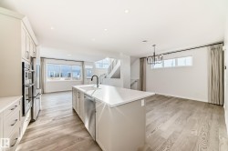 Kitchen with white cabinets, an island with sink, light wood-type flooring, appliances with stainless steel finishes, and hanging light fixtures - 