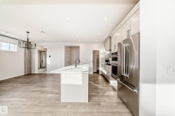 Kitchen featuring a center island with sink, stainless steel appliances, decorative light fixtures, light wood-style flooring, and recessed lighting - 