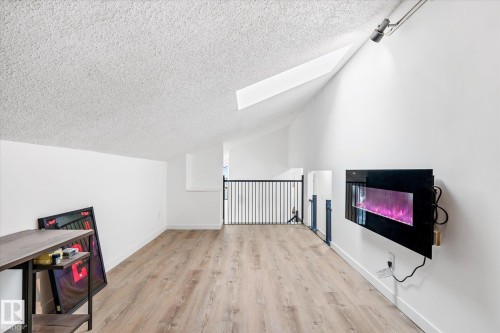 Bonus room with a textured ceiling, vaulted ceiling, light wood finished floors, a glass covered fireplace, and a skylight - 38 Woodcrest Avenue, St. Albert, AB - Indoor Photo Showing Other Room
