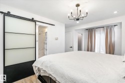 Bedroom featuring a barn door, light wood-style floors, a chandelier, and a textured ceiling - 