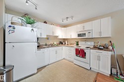 Kitchen with white appliances, white cabinetry, a textured ceiling, track lighting, and light flooring - 