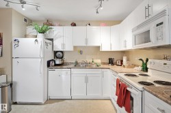 Kitchen featuring white appliances, white cabinetry, track lighting, and light countertops - 