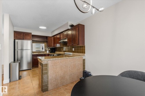 Kitchen featuring freestanding refrigerator, light tile patterned floors, a peninsula, backsplash, and dark brown cabinets - 289 Grandin Village, St. Albert, AB - Indoor Photo Showing Kitchen