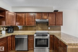 Kitchen with stainless steel appliances, tasteful backsplash, open shelves, light stone counters, and a textured ceiling - 