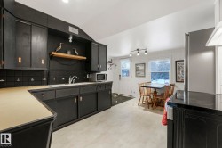 Kitchen featuring dark cabinetry, stainless steel appliances, light countertops, lofted ceiling, and open shelves - 