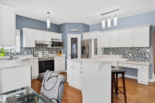 Kitchen featuring a breakfast bar, light countertops, stainless steel appliances, white cabinetry, and tasteful backsplash - 24 Olmstead Court, St. Albert, AB - Indoor Photo Showing Kitchen With Upgraded Kitchen