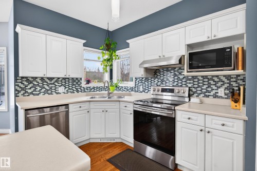 Kitchen with appliances with stainless steel finishes, white cabinetry, light countertops, and under cabinet range hood - 24 Olmstead Court, St. Albert, AB - Indoor Photo Showing Kitchen With Double Sink With Upgraded Kitchen