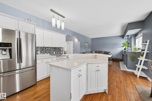 Kitchen featuring stainless steel refrigerator with ice dispenser, white cabinetry, open floor plan, light wood-type flooring, and light countertops - 24 Olmstead Court, St. Albert, AB - Indoor Photo Showing Kitchen