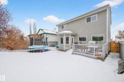 Snow covered house featuring a trampoline, a wooden deck, a fenced backyard, and a gate - 