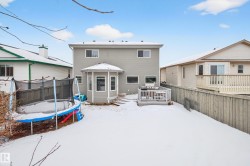 Snow covered rear of property with a trampoline, a deck, and a fenced backyard - 