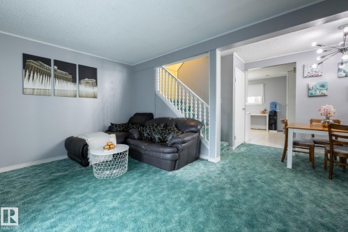 Carpeted living area featuring a textured ceiling, stairs, crown molding, and a chandelier - 1346 Lakewood Road W, Edmonton, AB - Indoor Photo Showing Living Room