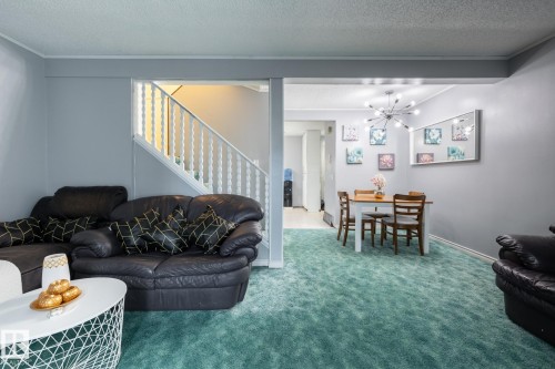 Carpeted living room featuring a textured ceiling, stairway, a chandelier, and ornamental molding - 1346 Lakewood Road W, Edmonton, AB - Indoor Photo Showing Living Room
