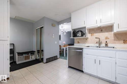 Kitchen featuring white cabinets, stainless steel dishwasher, light countertops, a chandelier, and tasteful backsplash - 1346 Lakewood Road W, Edmonton, AB - Indoor Photo Showing Kitchen With Double Sink